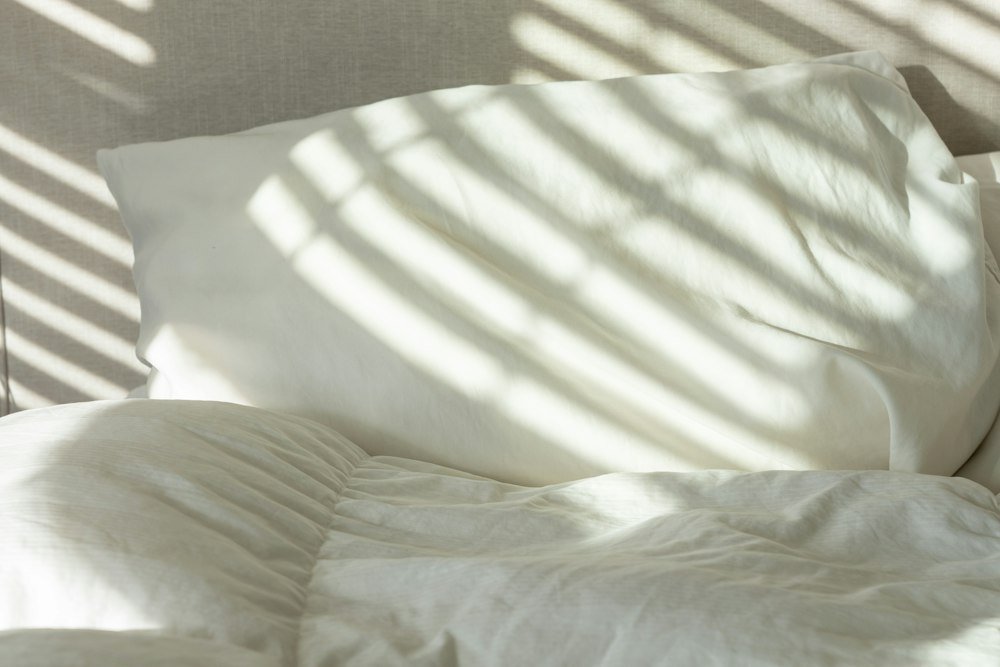 Bed with white sheets and pillows beside a bright window